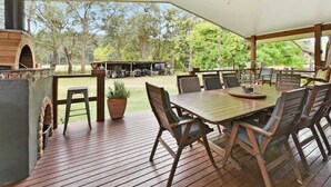 An outdoor patio with a wooden table and chairs, a ceiling fan, and a brick oven. - Laguna  Farmhouse Studio (Laguna)