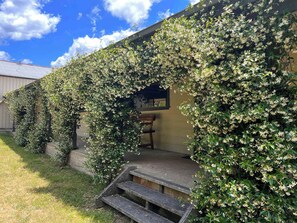 A building with a covered porch and steps leading up to it, surrounded by lush greenery and flowering plants. - Laguna  Farmhouse Studio (Laguna)