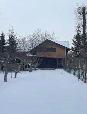 Une maison avec un toit en pente, entourée d’un paysage enneigé et d’arbres sans feuilles.
