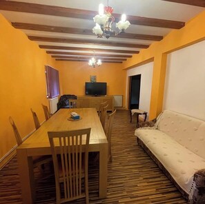 Un comedor con una mesa y sillas de madera, un sofá y un televisor sobre un mueble.