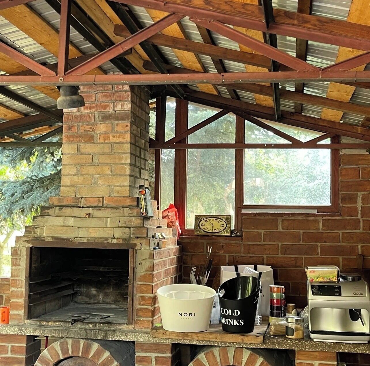 An outdoor kitchen area with a brick oven, a coffee machine, and a window overlooking greenery.