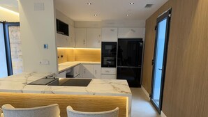 A modern kitchen with a marble countertop, two grey chairs, and built-in appliances.