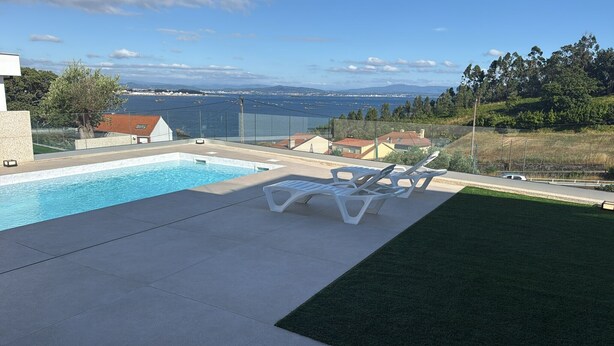 A swimming pool with lounge chairs, a view of a body of water, and a hilly landscape.