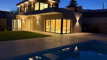 A modern two-story house with a swimming pool in the foreground.