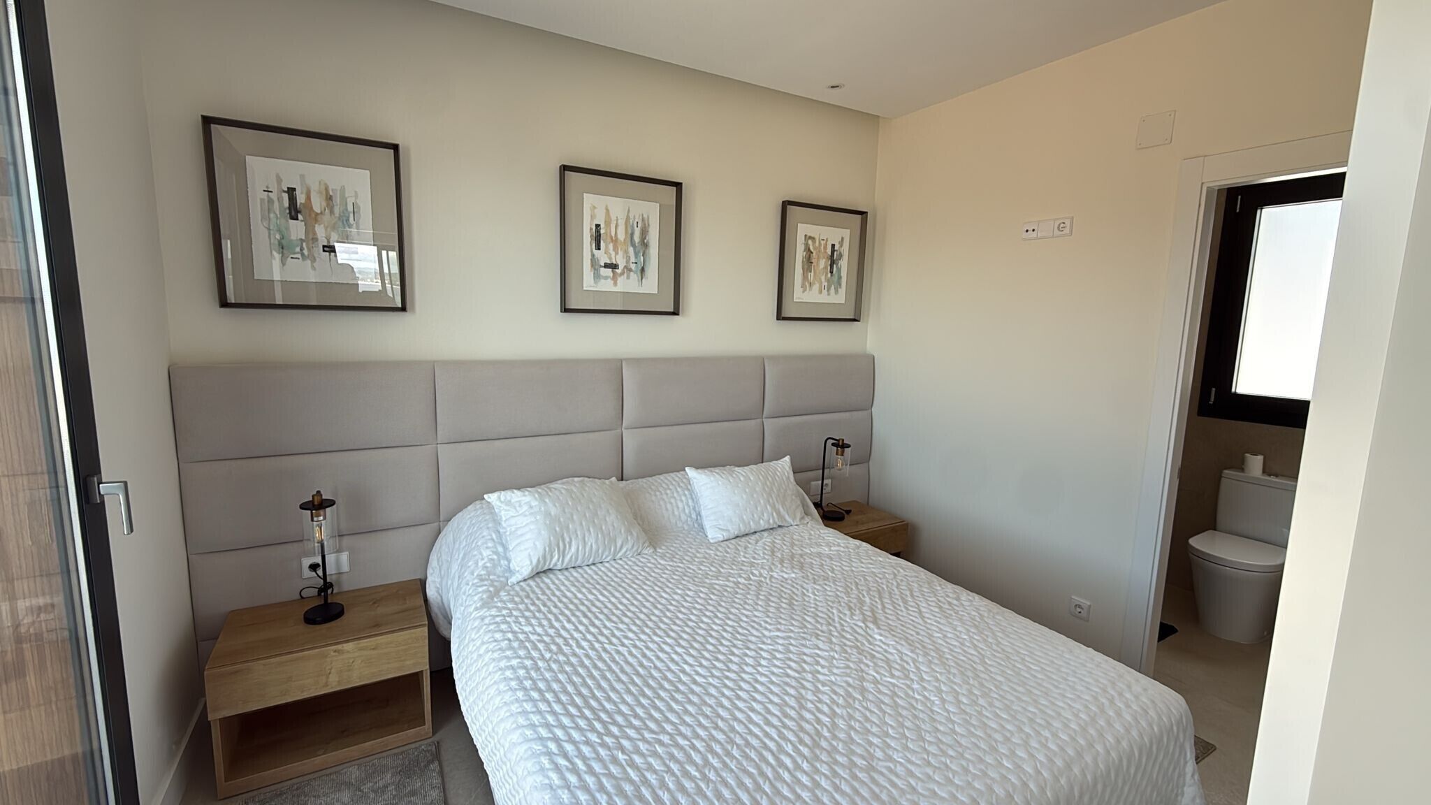 Een slaapkamer met een groot bed, twee nachtkastjes, een hoofdbord en drie ingekaderde foto's aan de muur.