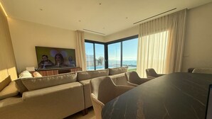 A modern hotel room with a large sofa, a dining table, and a TV mounted on the wall.