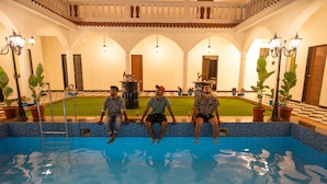 Three individuals seated on a poolside ledge with a tiled pool in the foreground.