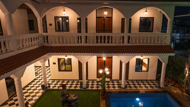 A hotel with a pool, checkered flooring, and a covered outdoor area with columns and a railing.