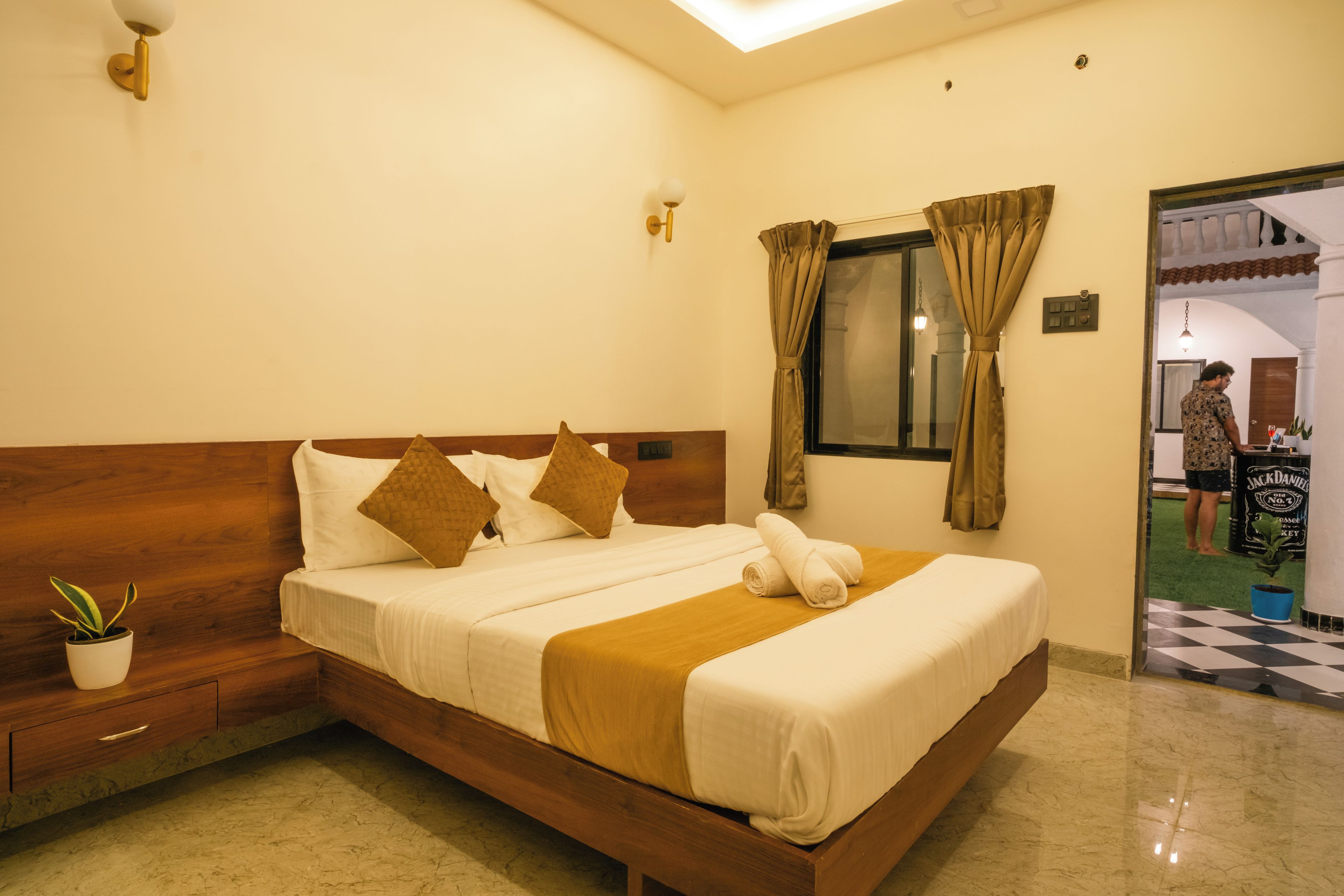 Habitación de hotel con una cama de madera, una planta en maceta y un ventanal con cortinas.