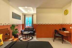 A hotel room with a bed, a desk, a chair, a sofa, a coffee table, and a potted plant.