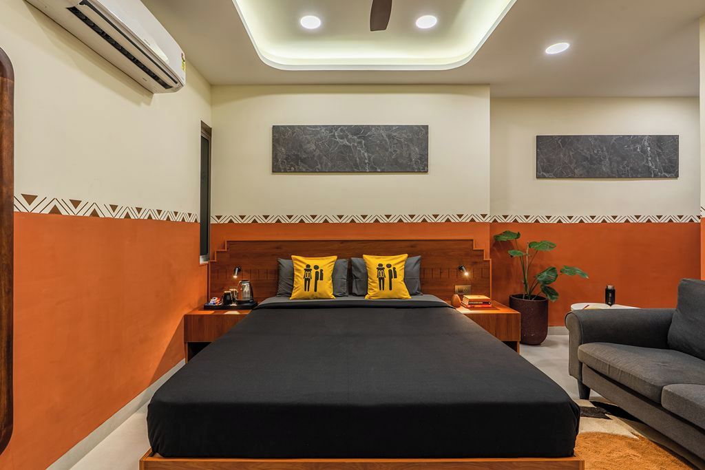 A hotel room with a large bed, two bedside tables, a nightstand, a sofa, and a potted plant.