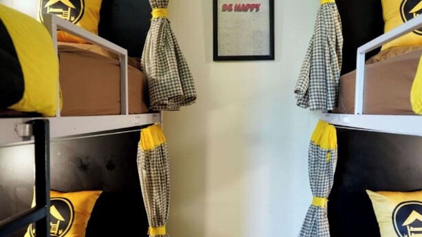Quarto com beliche, cortinas xadrez e almofadas amarelas com o logotipo de uma casa.