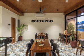 A conference room with a wooden table, chairs, a foosball table, a chessboard, and a wall-mounted air conditioning unit.