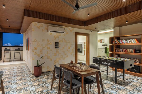 A room with a foosball table, a chessboard, and a bookshelf.