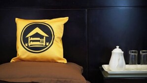 Cama com travesseiro marrom e um travesseiro amarelo com logotipo preto e branco.