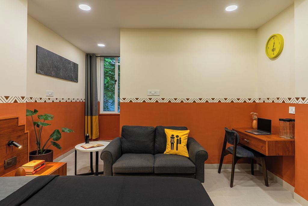 A compact room with a sofa, a small table, a desk, a bed, a clock, and a window.