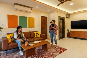 Una sala de estar moderna con un sofá, una mesa de centro con libros, un televisor y un ventilador de techo.