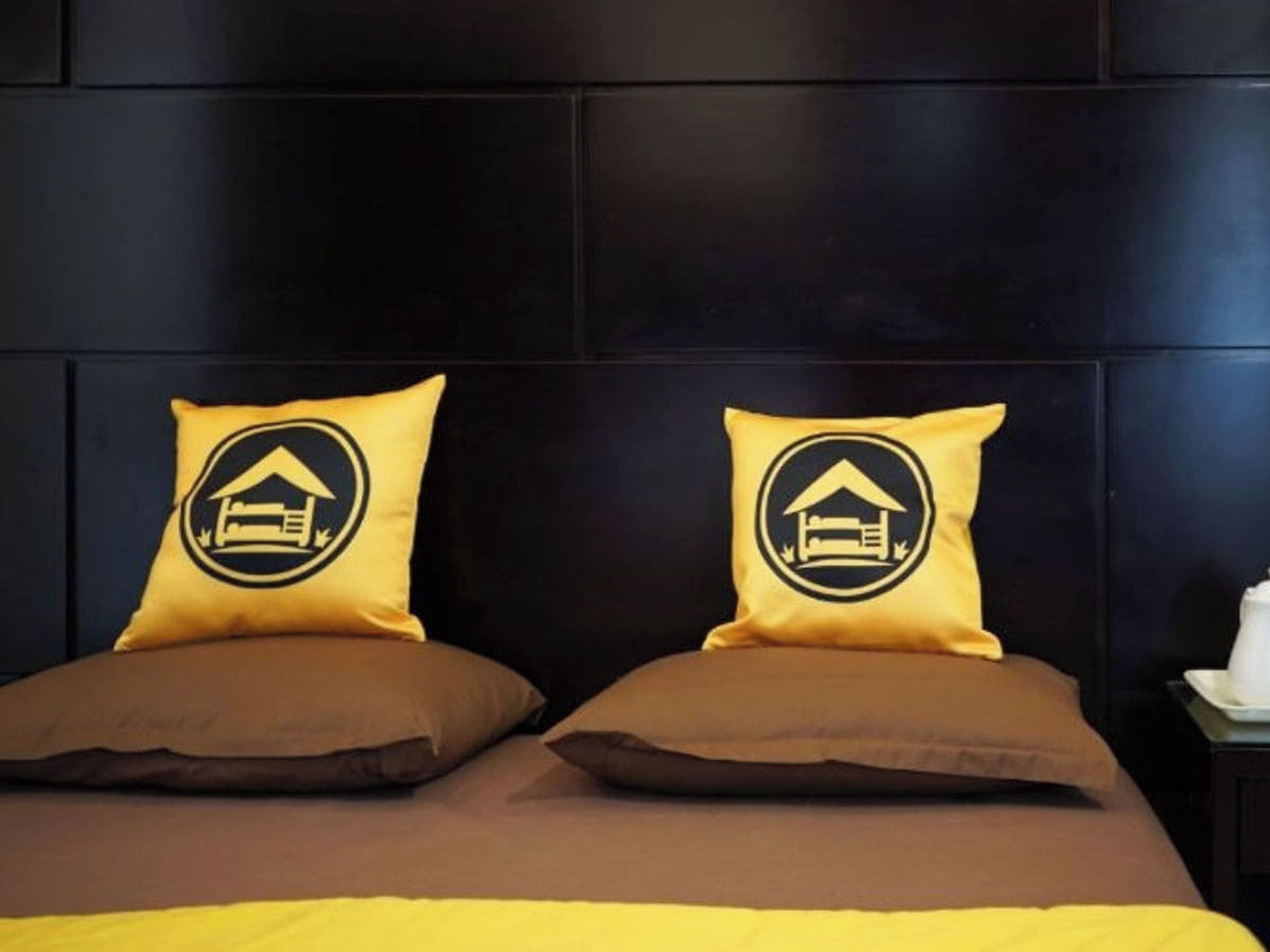 A bed with two pillows, one with a house logo and the other plain.