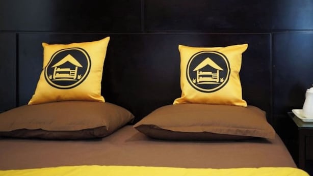 Uma cama com duas almofadas, uma com o logotipo de uma casa e outra sem detalhes.