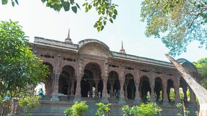 Um edifício histórico com várias arcadas e uma cúpula central, rodeado por um jardim bem cuidado.