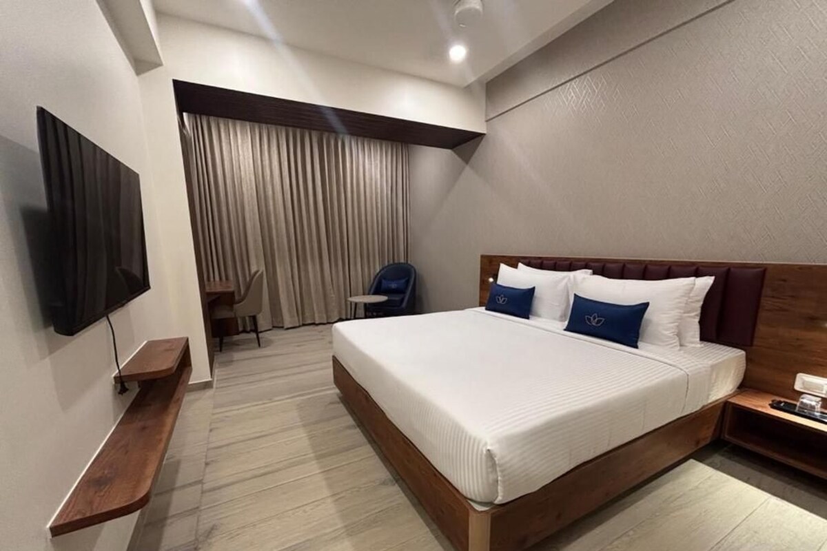 A hotel room with a bed, a TV mounted on the wall, a chair, and a desk.