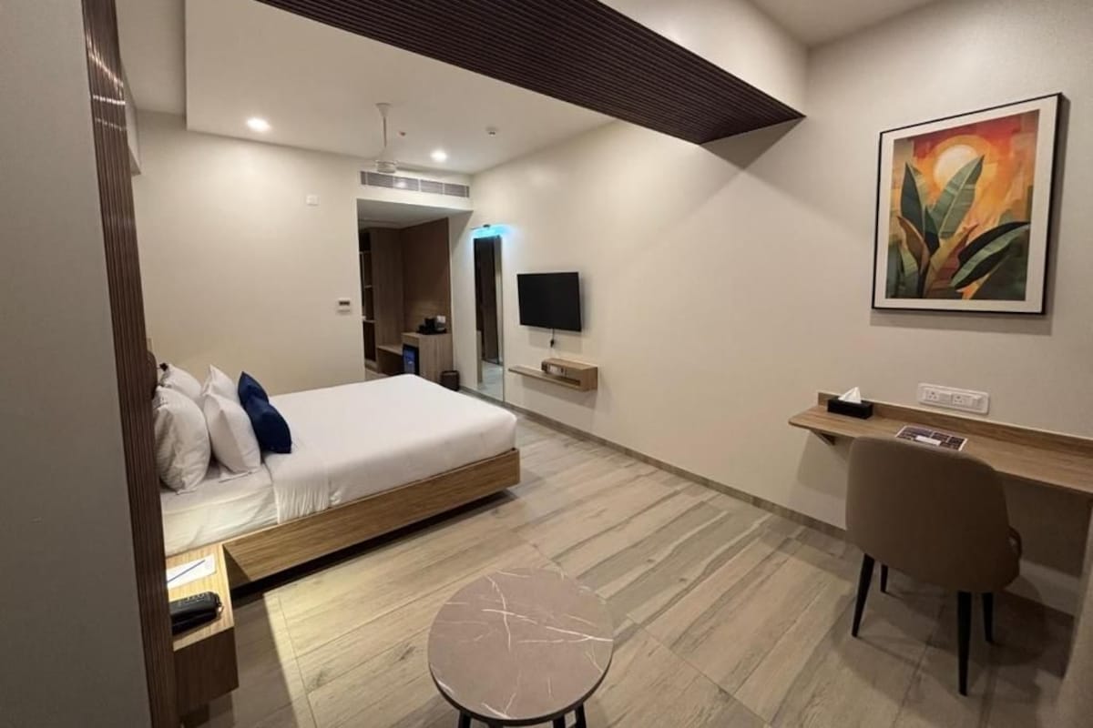 A modern hotel room with a bed, desk, chair, and artwork on the wall.