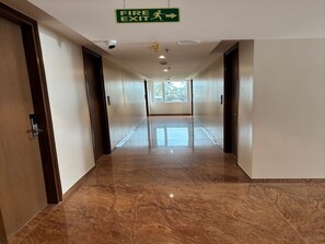 A hotel corridor with a fire exit sign, security cameras, and a window at the end.