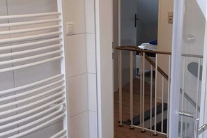 Ein Hotelzimmer mit einer weiß gefliesten Wand, Holzboden, einer Glastür zum Badezimmer und einem weißen Heizkörper.