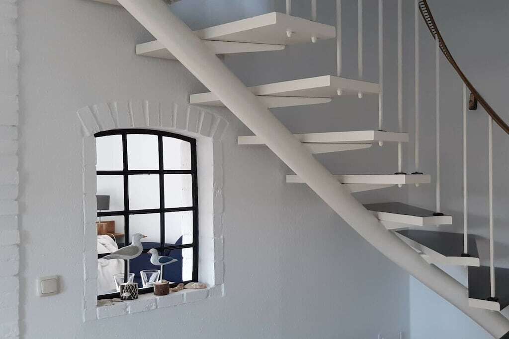 Un escalier en colimaçon blanc avec une fenêtre en bas.