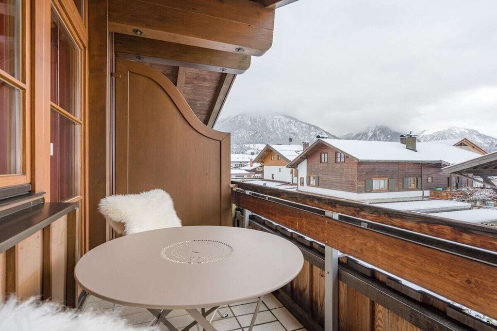 Un balcon avec une table ronde et une chaise blanche, donnant sur un paysage montagneux enneigé.