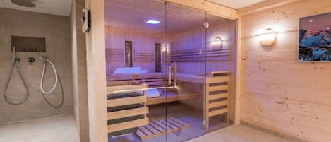 Et sauna rum med en glasafskærmning, træbænke, en bænk med et håndklæde og en fastgjort lysarmatur på væggen.