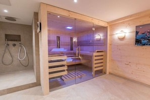 A sauna room with a glass partition, wooden benches, a bench with a towel, and a wall-mounted light fixture. - Holiday home with 4 bedrooms (Oberstdorf)