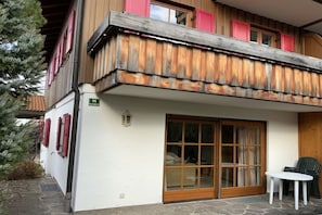 A two-story building with a balcony, a sliding glass door, and a small outdoor seating area. - Holiday home with 4 bedrooms (Oberstdorf)