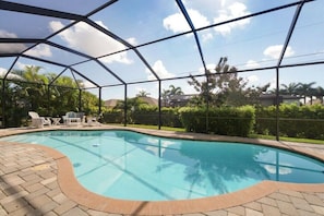 Ein Swimmingpool mit glatter, blauer Wasseroberfläche, umgeben von einer Ziegelterrasse und einem Metallzaun.
