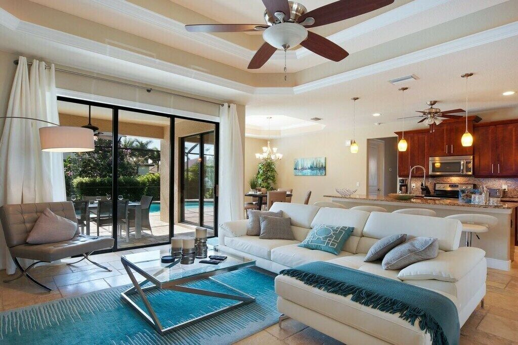 A spacious living room with a sofa, coffee table, and a dining area with chairs. There is a kitchen area with cabinets and a microwave.