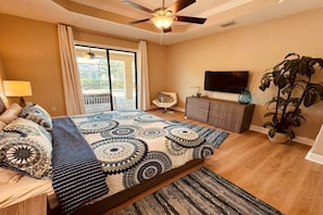 Ein Schlafzimmer mit Bett, Fernseher, Pflanze und Balkon.