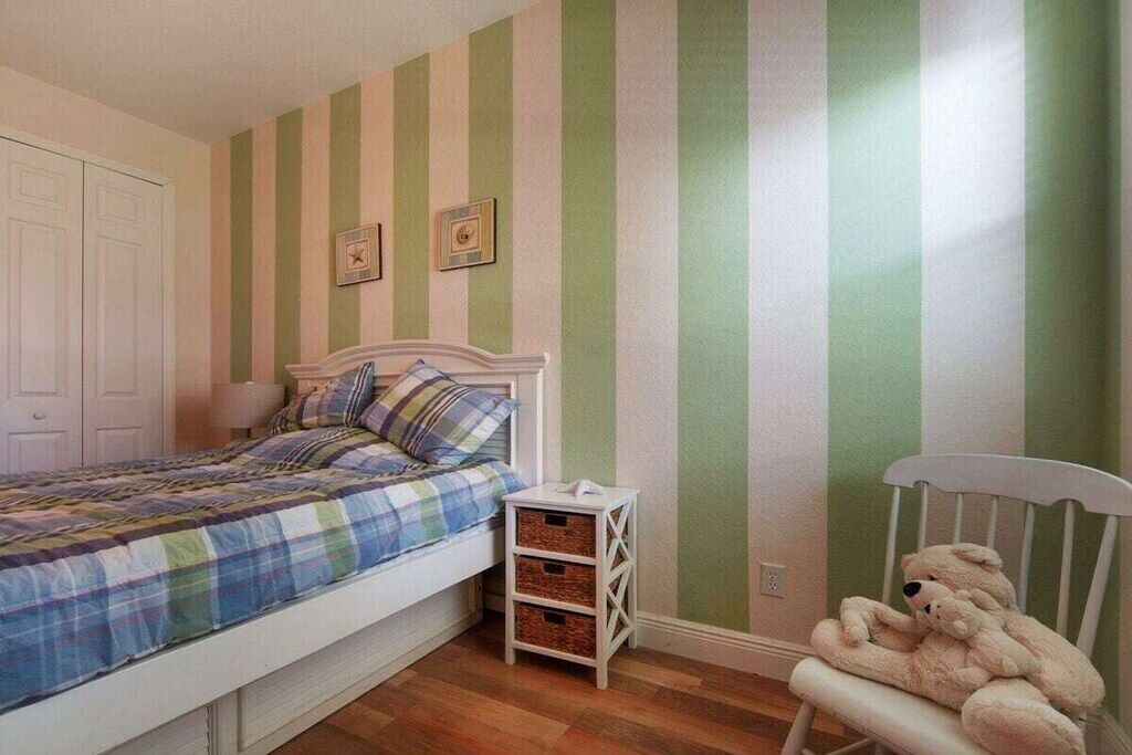 Une chambre à coucher avec un lit, une table de chevet et une chaise sur laquelle sont posés des animaux en peluche.