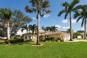 A residential property with a well-maintained lawn, palm trees, and a two-story house with a tiled roof. - CCVS - Villa Blue Water (Cape Coral)