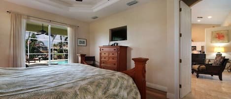 A bedroom with a bed, a ceiling fan, a wooden dresser, and a view of a pool through a sliding glass door.