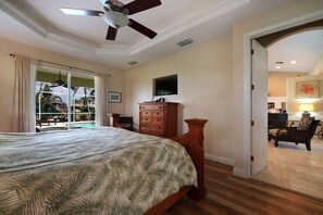 A bedroom with a bed, a ceiling fan, a wooden dresser, and a view of a pool through a sliding glass door. - CCVS - Villa Blue Water (Cape Coral)
