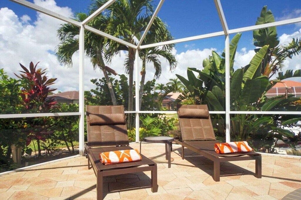 Un espace de détente extérieur, baigné de soleil, avec deux fauteuils confortables et une petite table, entouré de plantes tropicales et sous un ciel dégagé.