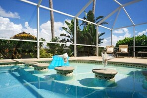 A pool area with clear blue water, surrounded by a white structure, and palm trees in the background. - CCVS - Villa Blue Water (Cape Coral)