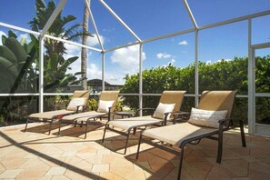 A sunlit outdoor seating area with four lounge chairs and a glass enclosure. - CCVS - Villa Blue Water (Cape Coral)