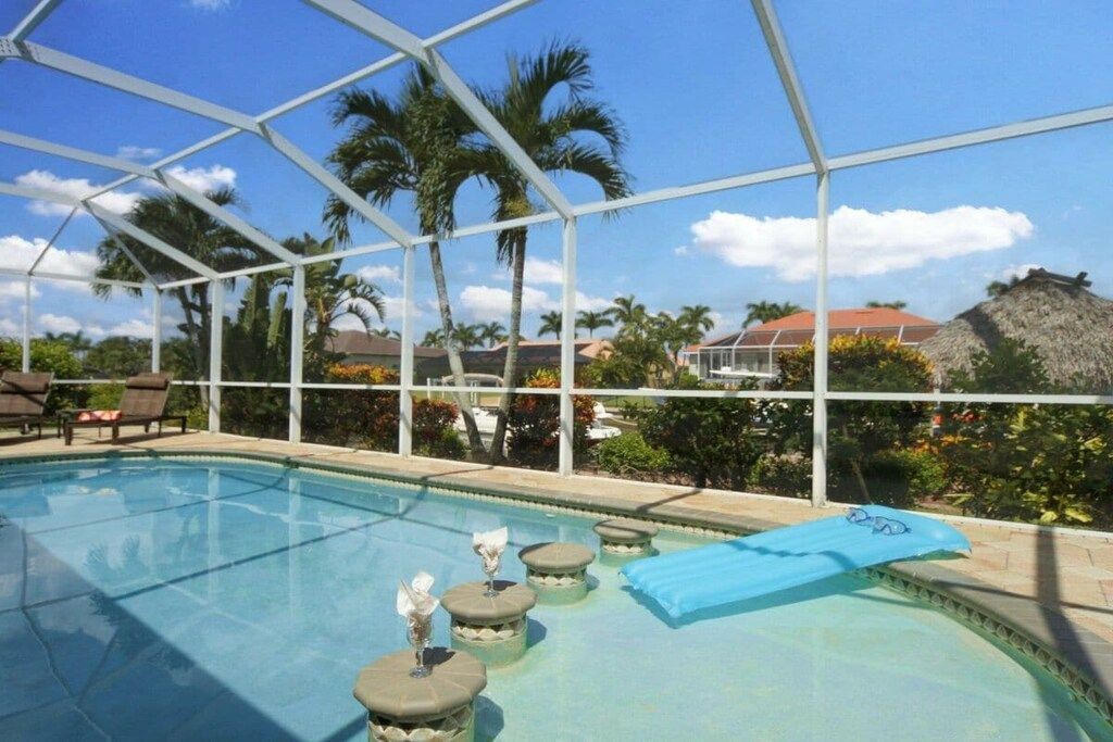 A pool area with a clear sky, palm trees, and a thatched-roof structure in the background.