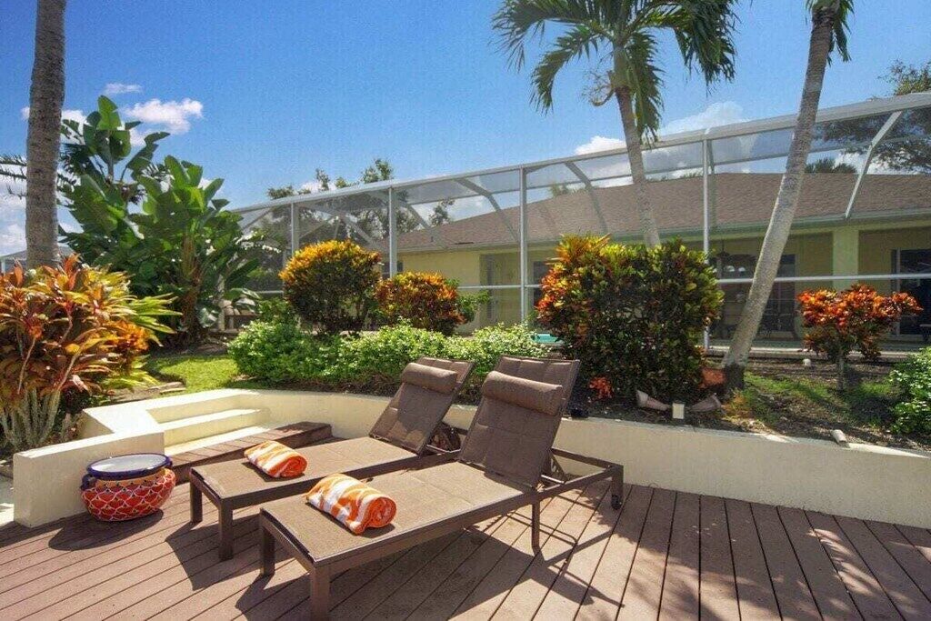 An outdoor deck with lounge chairs and a table, surrounded by tropical plants and a glass-enclosed structure.