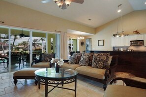 A spacious living room with a sofa, a glass coffee table, and a view of the outdoors. - CCVS - Villa Blue Water (Cape Coral)