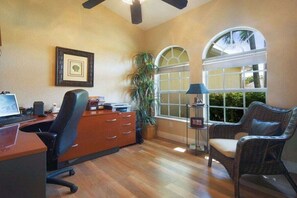 A room with a desk, chair, bookshelf, two windows, and a ceiling fan. - CCVS - Villa Blue Water (Cape Coral)