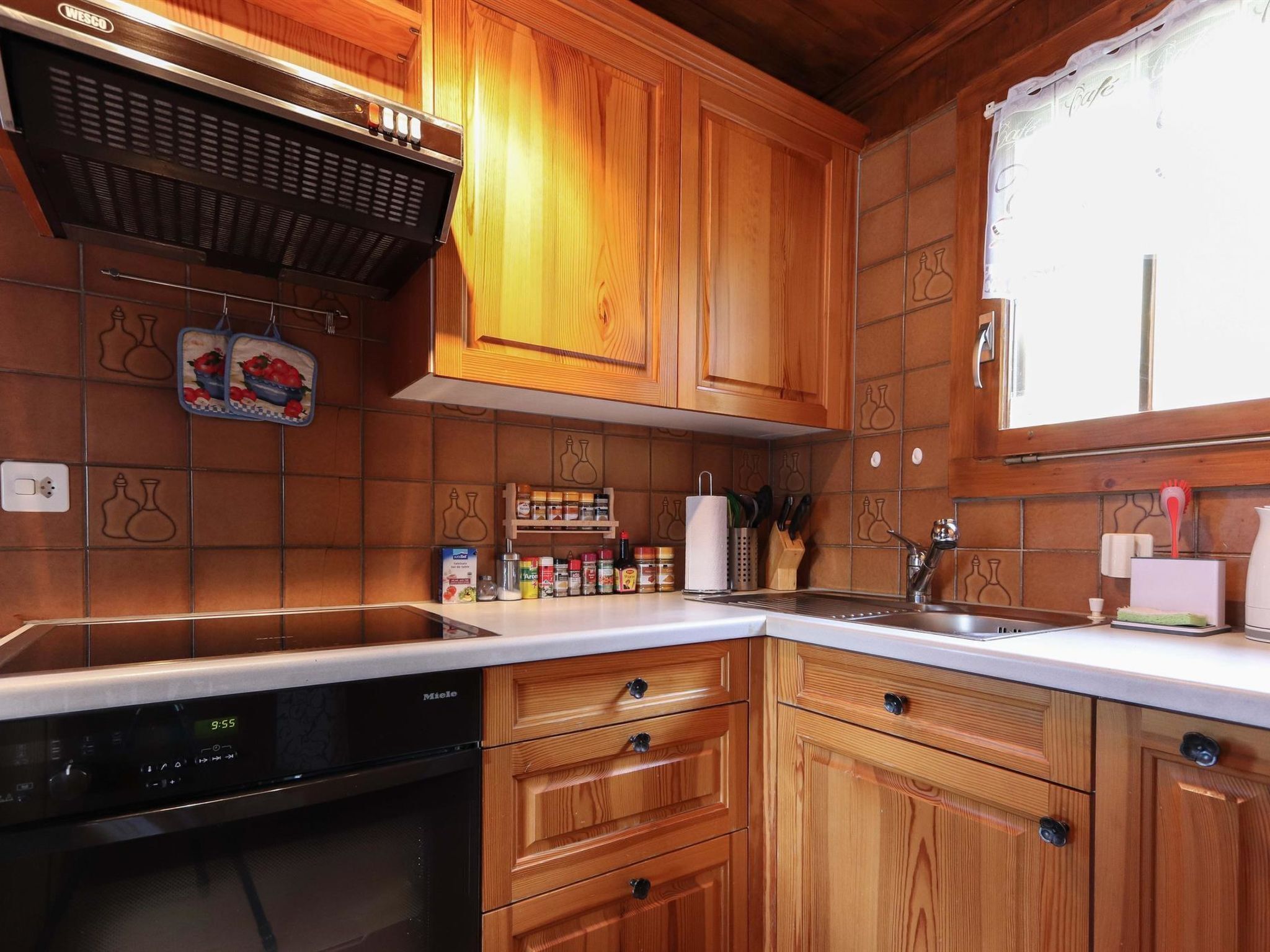 Una cocina con armarios de madera, lavavajillas integrado y una ventana con cortina.