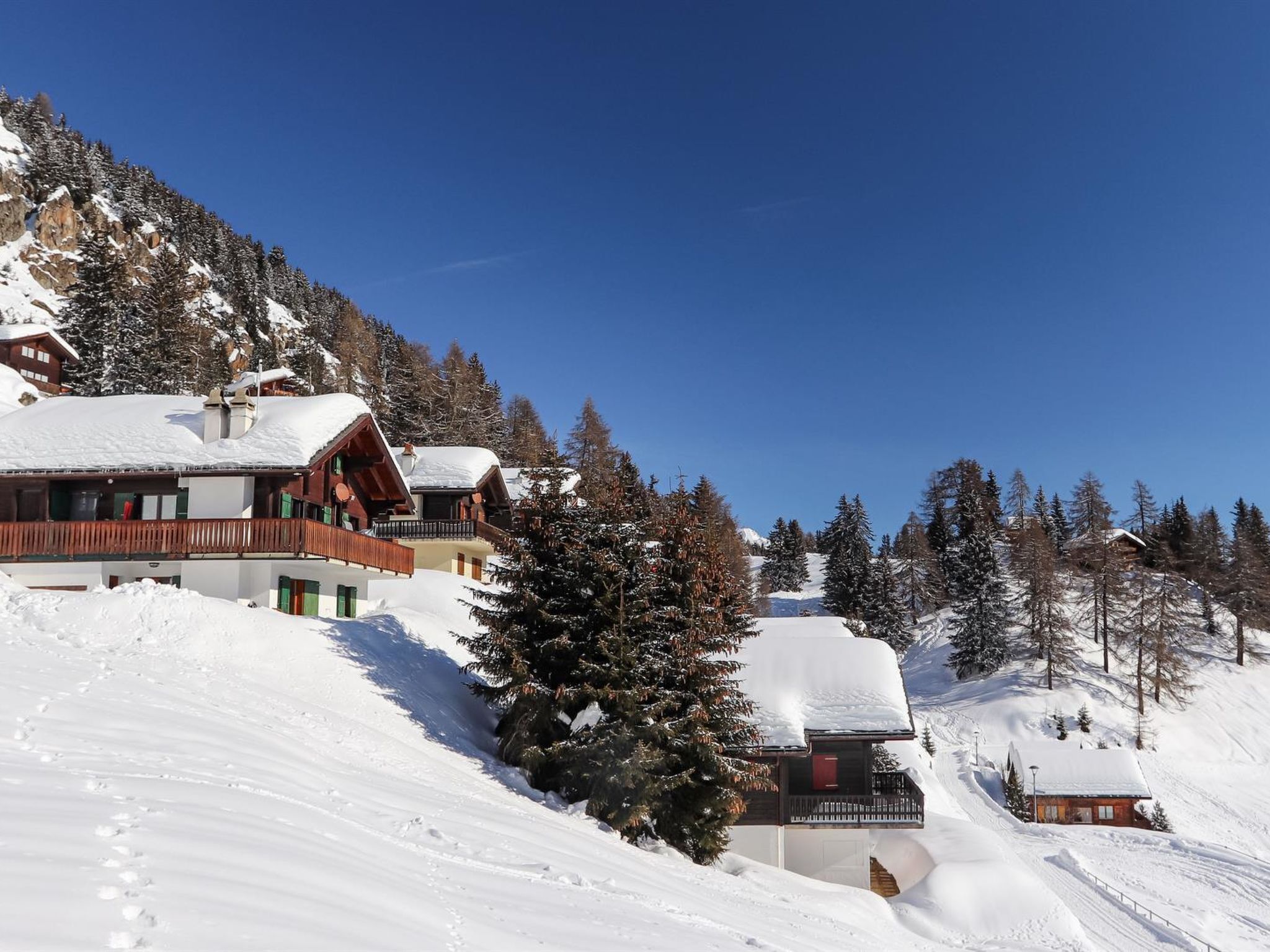 A snow-covered mountain area with wooden chalets and a ski slope.