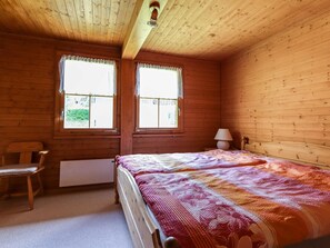 Una habitación de madera con una cama, una silla y dos ventanas.